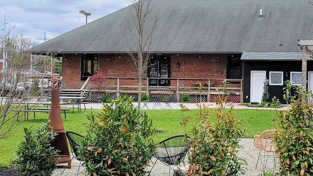 A brick building with a sloped roof, a fenced outdoor area with chairs, and a small tree. - A thoughtfully designed 3-bedroom, 2.5-bath townhome tailored for travelers. (Chambersburg)