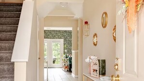 A hallway with a staircase, a console table with decorative items, and a door with a wreath. - A thoughtfully designed 3-bedroom, 2.5-bath townhome tailored for travelers. (Chambersburg)