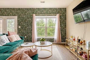 Ein Wohnzimmer mit einem grünen Sofa, einem runden Couchtisch und einem an der Wand befestigten Fernseher.