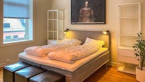 Ein Schlafzimmer mit Bett, Nachttischen, Fenster, einem Gemälde und einer Pflanze.