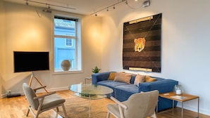 Ein modernes Wohnzimmer mit einem blauen Sofa, einem Glastisch und einem großen, abstrakten Gemälde.