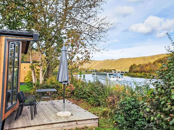 A wooden deck with a table and chairs, overlooking a river with a boat. - Tiny Haus Prinz Ludwig by Interhome (Riedenburg)