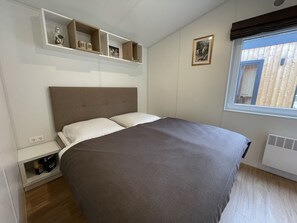 A bedroom with a bed, a window with blinds, a shelf with decorative items, and a wall-mounted picture. - Tiny Haus Prinz Ludwig by Interhome (Riedenburg)