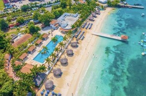 An aerial view of a coastal resort with a swimming pool, beach umbrellas, and a pier extending into the water. - Timeless 2BD&2BTH Gated Community @ Discovery Bay (Discovery Bay)