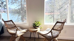 Ett rum med två flätade fåtöljer som står mittemot varandra, ett litet runt bord med en växt och stora fönster som ger utsikt över träd och en vattenyta.
