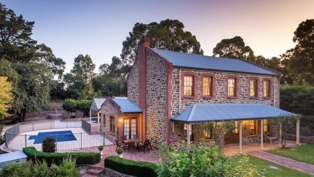 A stone house with a pool, covered patio, and landscaped garden.