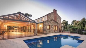 A house with a swimming pool, stone exterior, and a covered patio area.