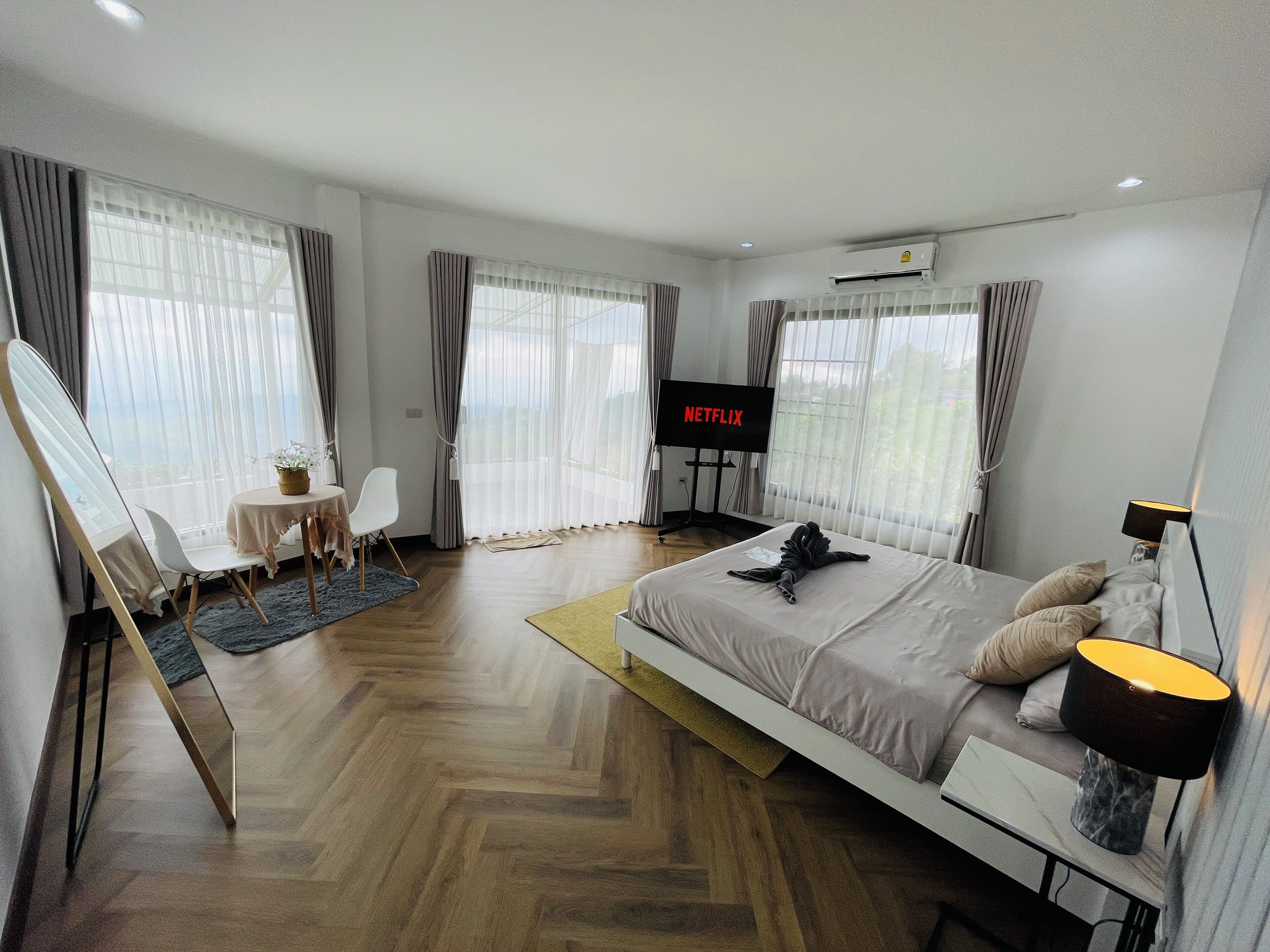 Een moderne hotelkamer met een groot bed, een bureau met stoel, een televisie en grote ramen met gordijnen.