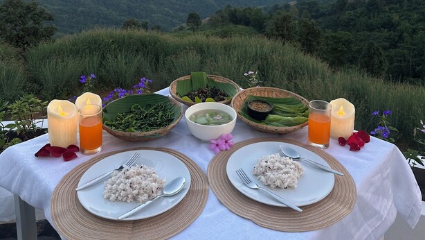 A table set for two with plates of rice, a bowl of soup, and two glasses of orange juice, surrounded by candles and a view of a mountainous landscape. - Above the clouds - Chiang rai (Chiang Rai)