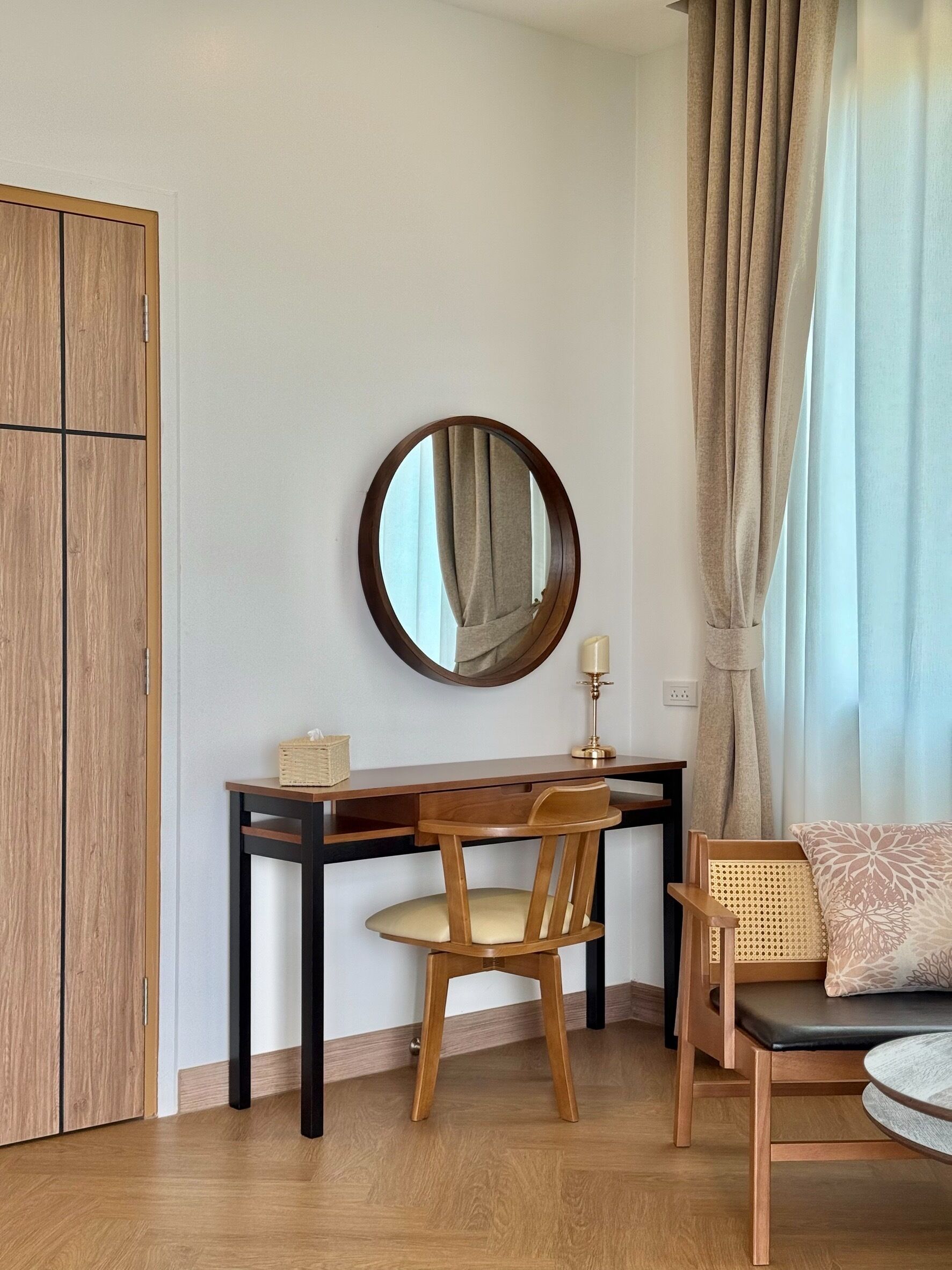 A room with a wooden desk, two chairs, a mirror, a lamp, and a window with curtains.