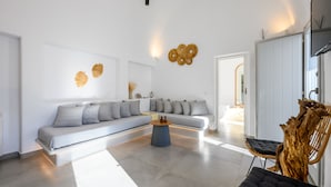 A modern living room with a sectional sofa, a round coffee table, and a wooden chair. - Hypnōs boutique villa with amazing heated pool hot tub (Santorini)