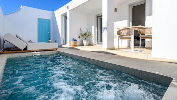 A swimming pool with a lounge chair and a table with chairs, surrounded by a white building with a blue door. - Hypnōs boutique villa with amazing heated pool hot tub (Santorini)
