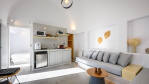 A modern kitchen with white cabinets, a microwave, and a coffee machine. There is a grey sofa with cushions and a round coffee table. - Hypnōs boutique villa with amazing heated pool hot tub (Santorini)
