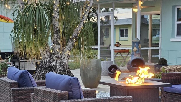 An outdoor seating area with wicker furniture, a fire feature, and a large planter with a hibiscus plant.