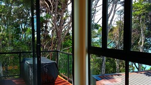 Un balcon donnant sur une forêt dense et une terrasse en bois.