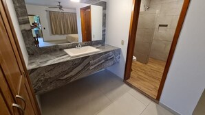 Un baño con encimera de mármol, lavamanos, espejo y zona de ducha.