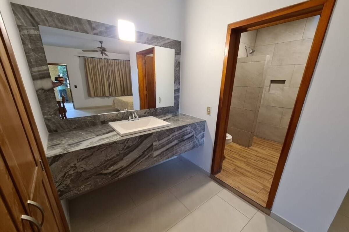 A bathroom with a marble countertop, a sink, a mirror, and a shower area.