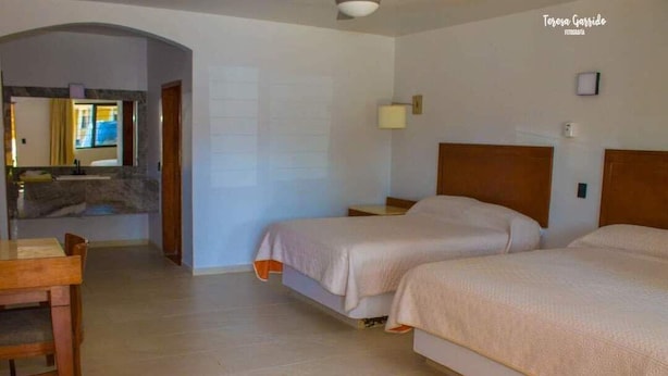 Habitación de hotel con dos camas, una mesita, una lámpara y vistas a un muro de piedra y una ventana.