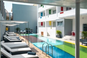 Ein Poolbereich auf dem Dach mit Liegestühlen und freiem Blick auf ein mehrstöckiges Gebäude mit Balkonen.