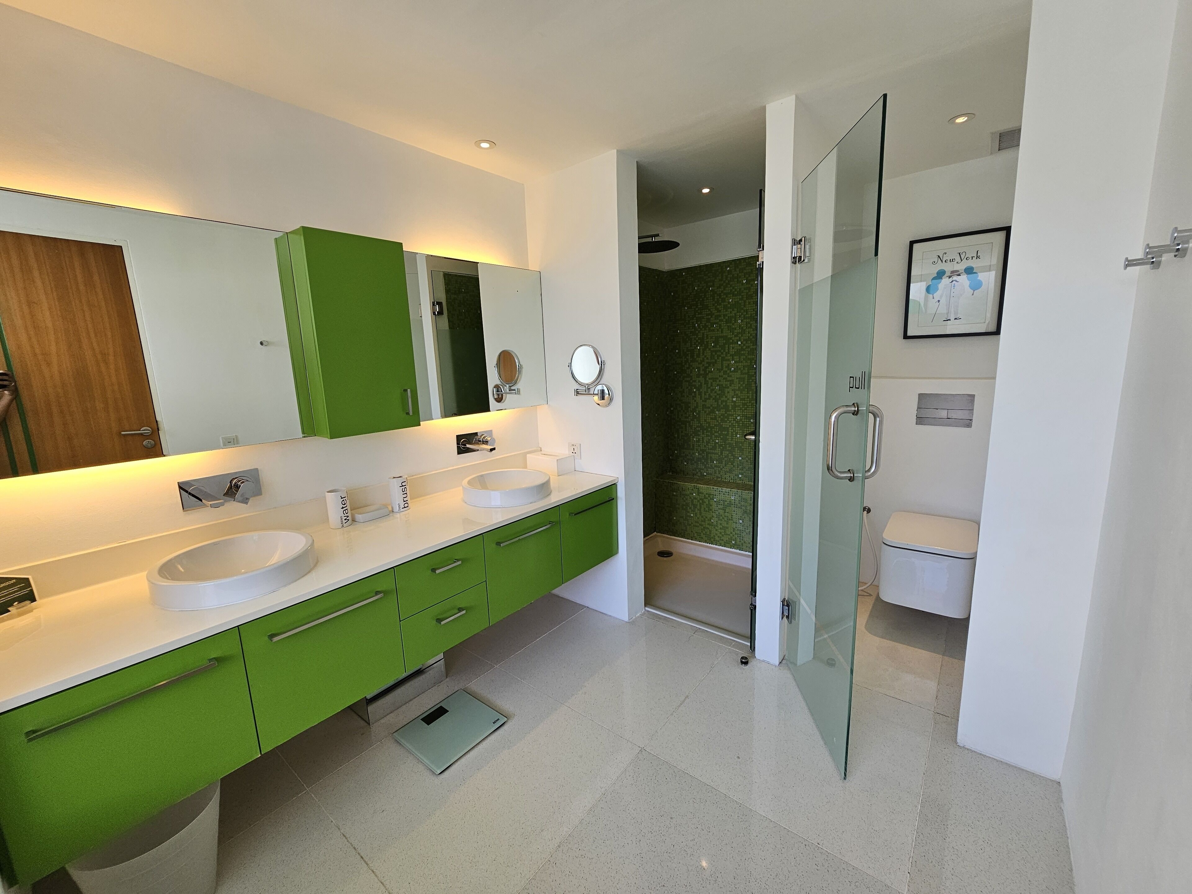 Une salle de bain moderne avec deux lavabos, des meubles verts, une douche en verre et des toilettes.