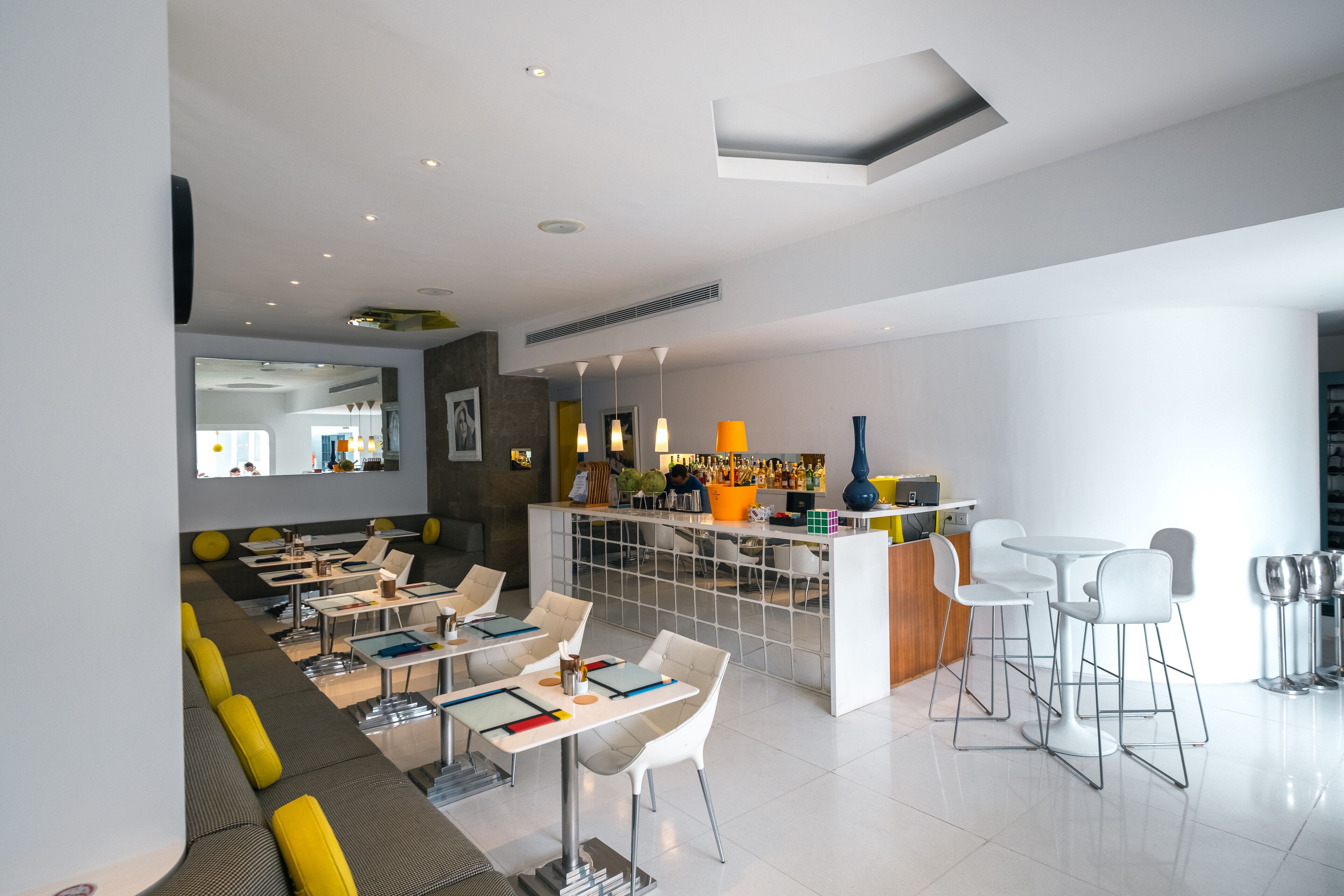 Um restaurante moderno com área de bar, diferentes disposições de assentos e um balcão visível com um bartender.