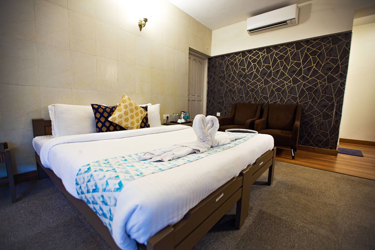 A neatly made bed with a patterned bedspread, a bedside table with a lamp, and a wall-mounted air conditioner.