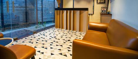 A reception area with a modern design, featuring a patterned floor, leather seating, and a glass wall providing a view of the outside.