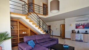 Un amplio salón con un sofá seccional color púrpura, una mesa de centro negra y una escalera con barandillas de madera.