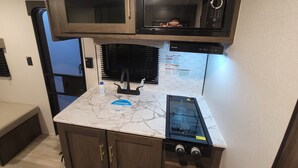 A compact kitchen with a microwave, stove, and cabinets. - Cozy RV Getaway for Couples! (Shelby)