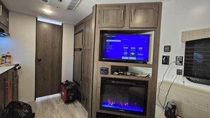 A modern kitchen with wooden cabinets, a built-in TV, and a fireplace. - Cozy RV Getaway for Couples! (Shelby)