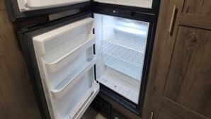 A compact refrigerator with multiple shelves and a freezer compartment, built into a wooden cabinet. - Cozy RV Getaway for Couples! (Shelby)