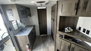 A compact kitchen with wooden cabinets, a countertop, and a built-in microwave. - Cozy RV Getaway for Couples! (Shelby)
