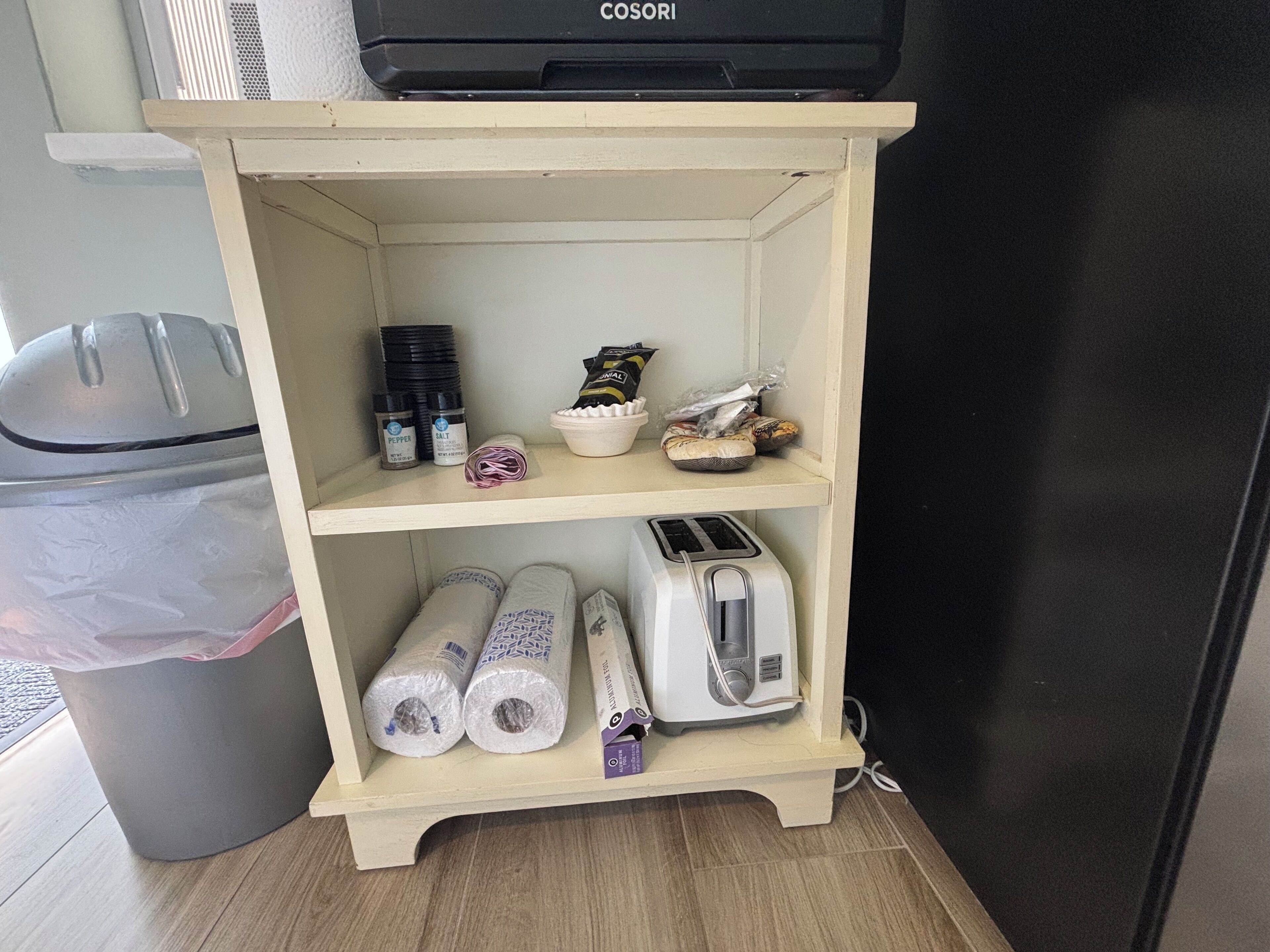 Ein kleines Holzregal mit verschiedenen Gegenständen, darunter ein Toaster, Pfeffer- und Salzbehälter, eine Schüssel und verpackte Waren.