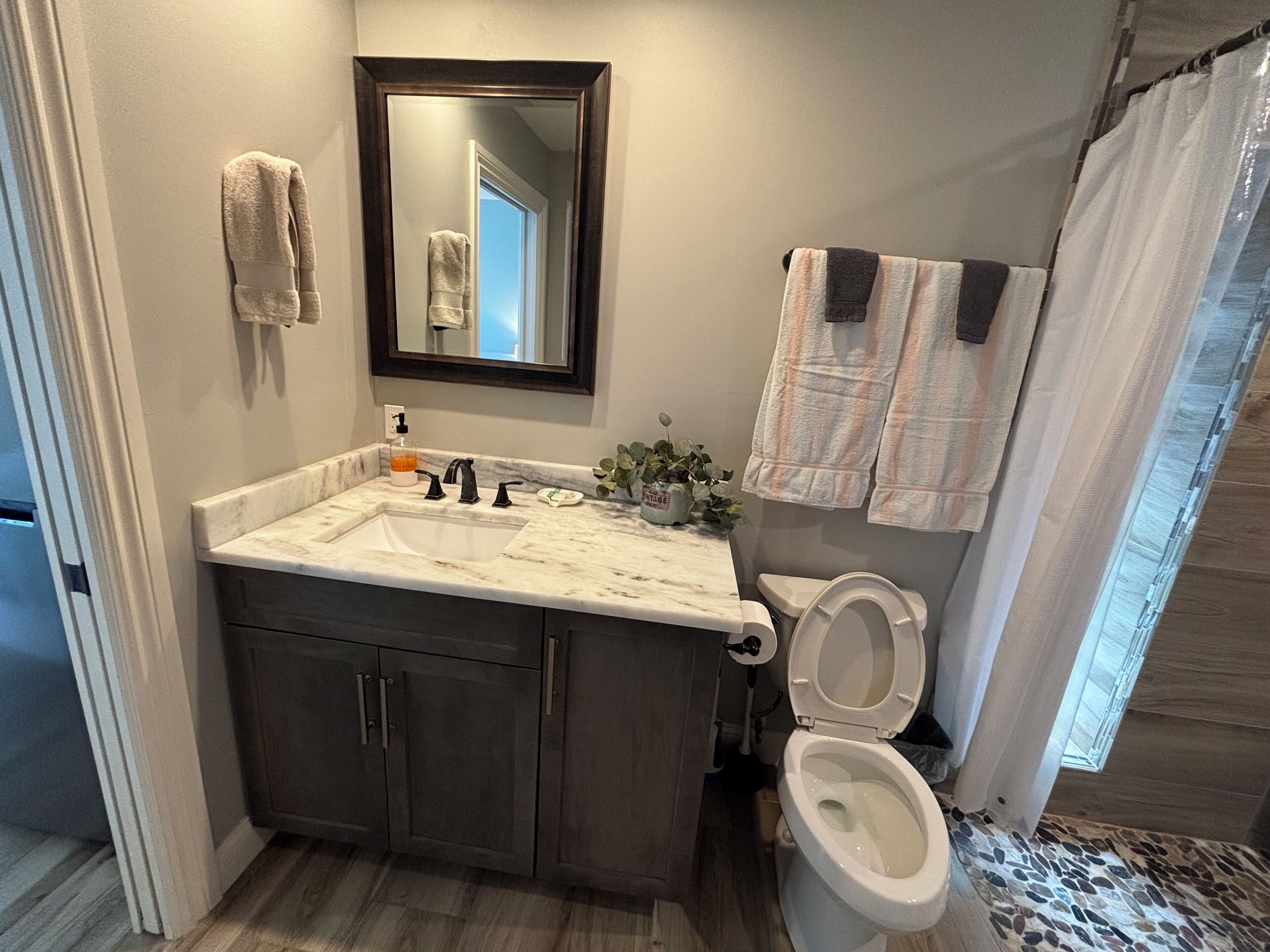 Un bagno con lavabo in marmo, mobili scuri, un water e una tenda per la doccia.
