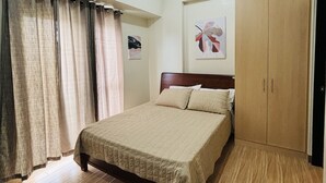 A bedroom with a bed, an air conditioner, a wardrobe, and a painting on the wall. - Megaworld Iloilo Condo Unit (Quezon City)