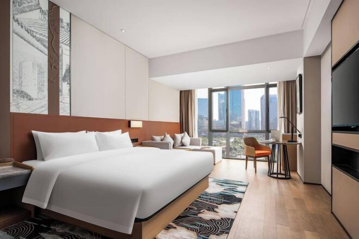 A modern hotel room with a large bed, a desk, a chair, and a TV.