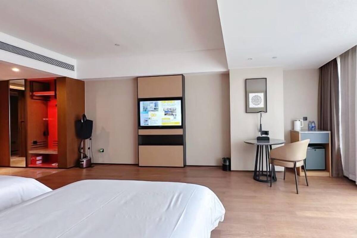 A hotel room with a bed, a desk, a chair, a television, and a wardrobe.