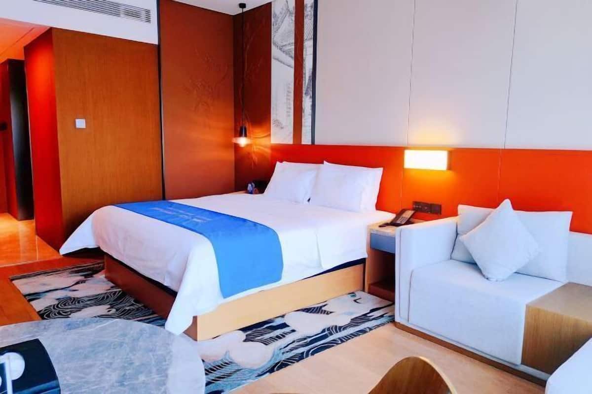 A hotel room with a bed, a sofa, a nightstand, and a wall-mounted phone.