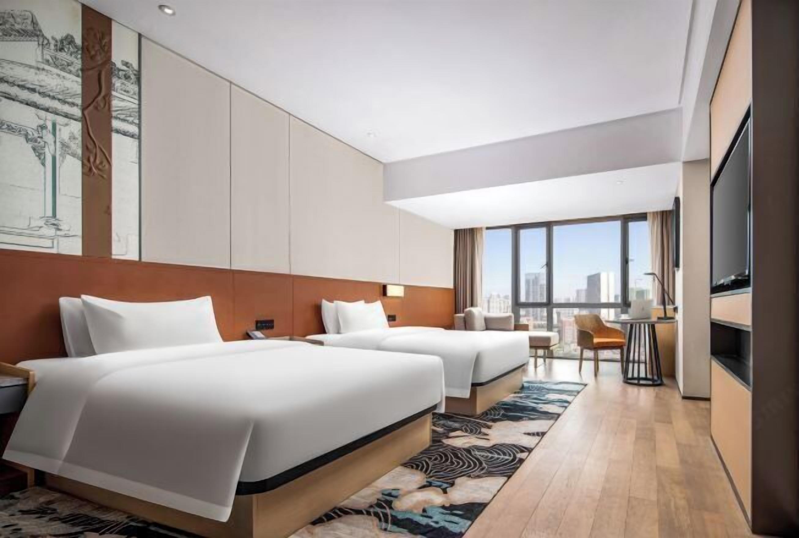 Een moderne hotelkamer met twee bedden, een zithoek en een groot raam met uitzicht op de stad.
