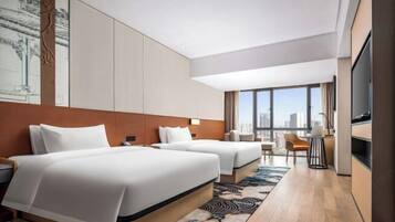 Een moderne hotelkamer met twee bedden, een zithoek en een groot raam met uitzicht op de stad.