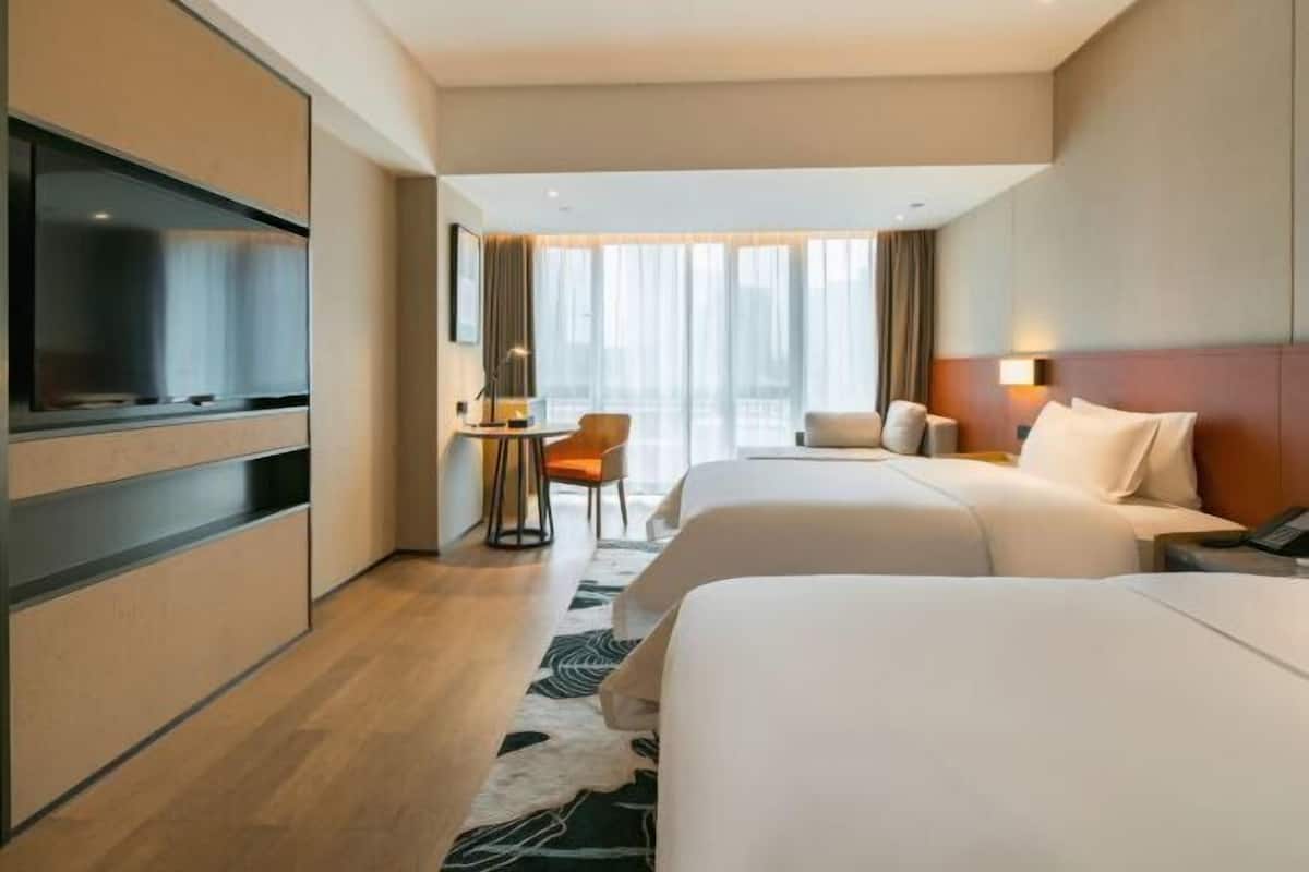 A hotel room with a bed, a desk, a chair, a TV, and a large window.
