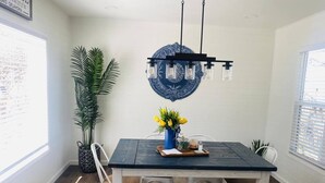 Zona pranzo con tavolo in legno, sedie, un elemento decorativo blu al muro e una lampada a sospensione.