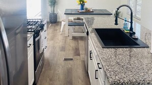 Una cucina moderna con un frigorifero in acciaio inossidabile, un piano cottura a gas, un ripiano in granito, un lavandino con un rubinetto nero e un elemento decorativo blu a parete.