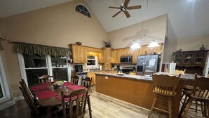 Una cocina amplia con armarios de madera, un comedor con mantel rojo y un ventilador de techo.