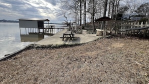 Un muelle junto al lago con banco de madera y mesa de picnic, un cobertizo pequeño y un pabellón.