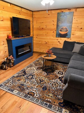 A cozy living room with a television, fireplace, sofa, and patterned rug. - Cozy Cabin 3 BR Fire Pit Peaceful Location King Beds (Sevierville)