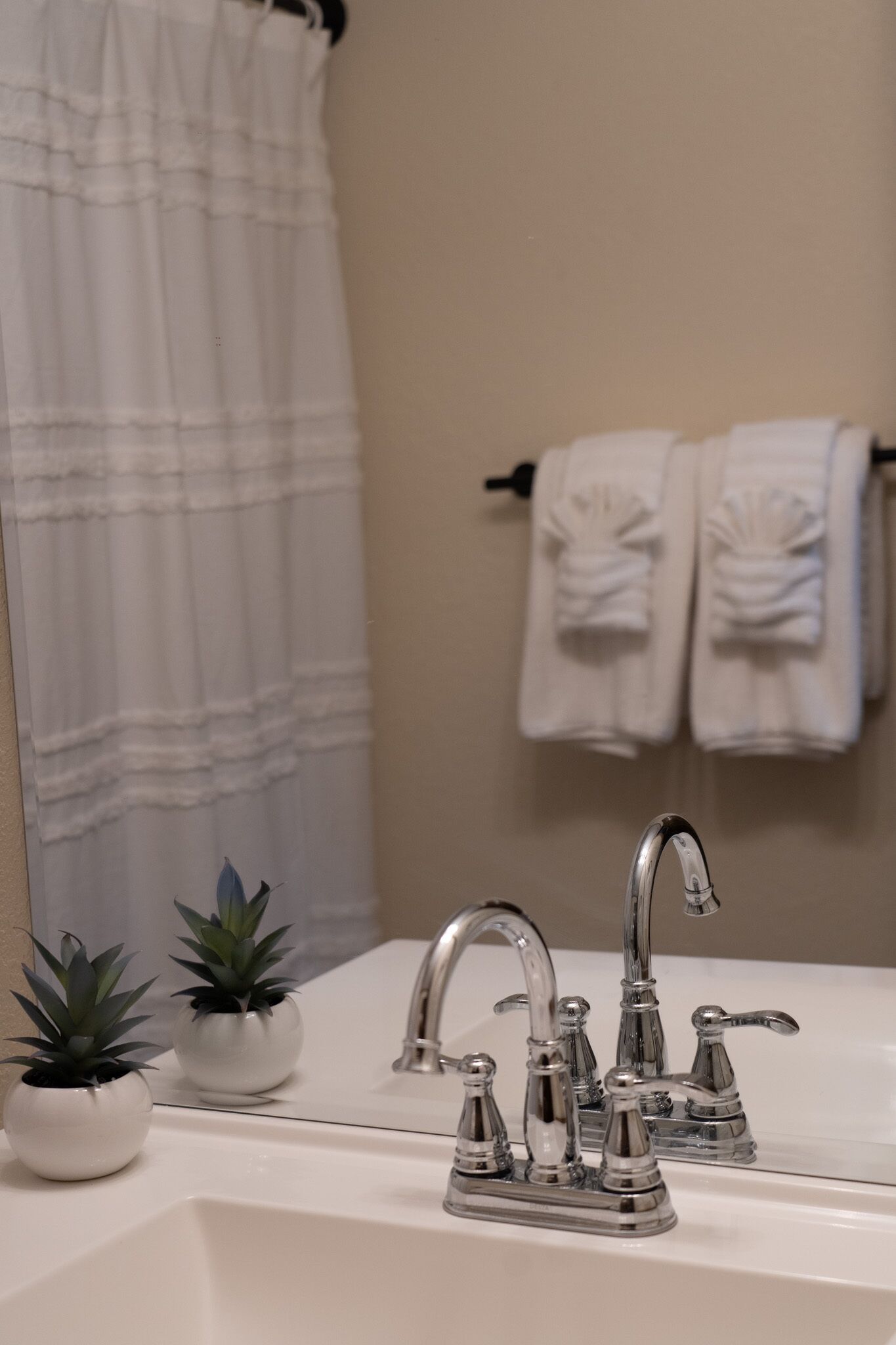 A bathroom with a white sink, a mirror, two potted plants, and two towels hanging on a rack.