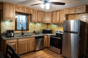 A kitchen with wooden cabinets, stainless steel appliances, a dishwasher, and a ceiling fan. - Cozy Cabin 3 BR Fire Pit Peaceful Location King Beds (Sevierville)