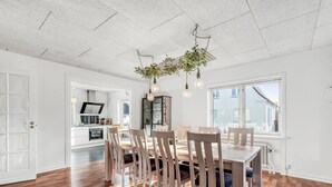 A spacious dining area with a wooden table and chairs, a kitchen in the background, and a large window providing natural light. - "Ullakarin" - 200m from the sea by Interhome (Thyborøn)