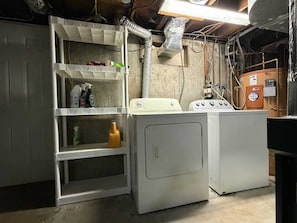 A laundry room with a washing machine, dryer, and shelves with cleaning supplies.